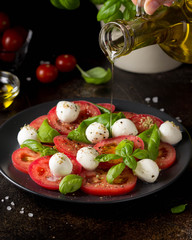 Caprese salad with mini mozzarella, juicy tomato and fresh Basil. Delicious Italian snack, traditional food. On dark background