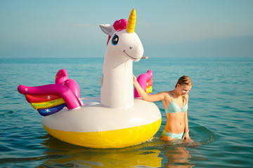 Lifestyle portrait of young beautiful girl with inflatable pool unicorn at sunset