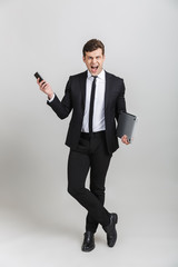 Sticker - Full length image of furious businessman in formal suit screaming while holding cellphone and laptop