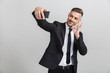 Image of successful smiling businessman in formal suit gesturing ok sing while taking selfie on cellphone