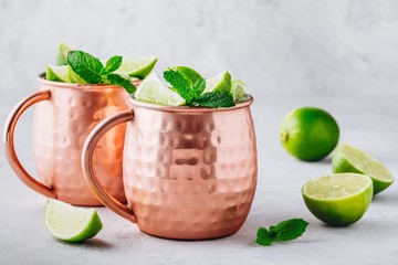 Wall Mural - Moscow mule ice cold cocktail in copper cup with lime and and mint on gray stone background