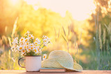 beautiful daisies in white cup, book, braided hat in summer garden. Rural landscape natural background with Chamomile flowers in sunlight. Summer time. copy space beautiful daisies in white cup, book, braided hat in summer garden. Rural landscape natural background with Chamomile flowers in sunlight. Summer time. copy space