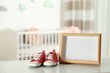 © New Africa - Photo frame and bootees on table in baby room interior. Space for text