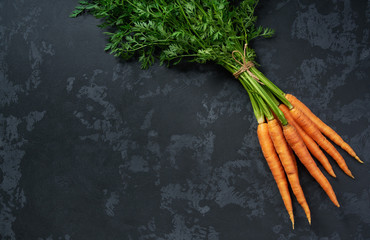 Bunch of fresh carrots on black background, top view.