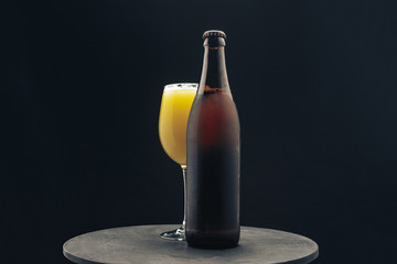 Poster - Glass of beerand brown Bottle on a dark round wooden table and black background behaid.