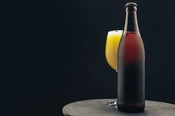 Poster - Glass of beerand brown Bottle on a dark round wooden table and black background behaid.