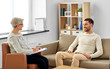 psychology, mental therapy and people concept - smiling senior woman psychologist with clipboard talking to young man patient at psychotherapy session