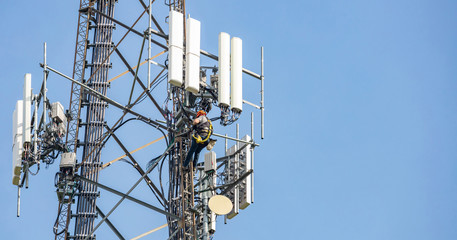 Telecom maintenance. Man climber on tower against blue sky background