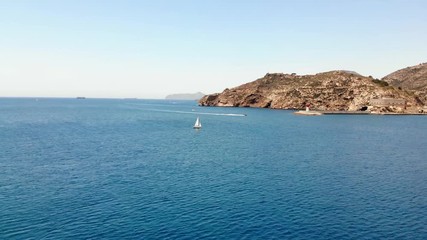 Wall Mural - The port entrance with lighthouse in front of the Spanish city of Cartagena. A sailboat and a motorboat are on the water. Aerial view in the sunshine and blue sky.