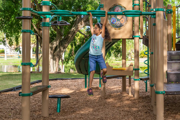 The young girl decides on her next move on the bars crossing over at the outdoor jungle gym. Focused on where to place her hands as she moves onto the middle top of the overhead bars.