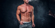 Handsome bodybuilder is smoking at dark studio, while posing for photographer.