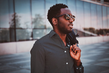 Wall Mural - Portrait of pensive modern afro man with sunglasses and blazer in his hands.