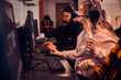 © Fxquadro - Focused girl get exited about videogame. She is wearing head set and glasses. another gamers at background.