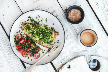 Wall Mural - Healthy vegan lunch. Flat-lay of avocado toast on sourdough bread with chives, coriander, cherry-tomatoes with cup of coffee over white background, top view. Vegetarian, clean eating concept