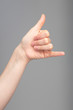Hand and arm of a Caucasian person is seen close-up and isolated against a grey background. Giving the call me hand gesture. Business contact and modern lifestyle concepts.
