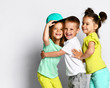© FAB.1 - Studio portrait of children on a light background: full body shot of three children in bright clothes, two girls and one boy. Triplets, brother and sisters. hugging on camera. Family ties, friendship