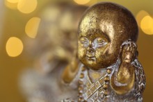Monk Figurine. I Do Not Hear,  Concept. Golden Monk Figurine  On Golden Background With Blurred Golden Bokeh.The Religion And The Motto Of Life.Statues With Emotions