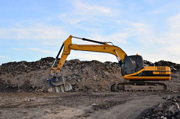 Canvas Print - A heavy excavator in a working at granite quarry unloads old concrete stones for crushing and recycling to gravel or cement. Special heavy construction equipment for road construction.