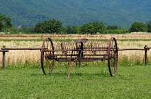 Antique Farm Equipment, An Hay Rake Machinery, On A Grass In Front Of A Wheat Field