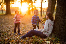 A Working Mother Playing With Kids During Sunset In An Autumn Park