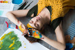 © golubovy - Leisure and recreation. Top view of peaceful female artist lying down on floor with her eyes closed, hands dirty with colorful paint.