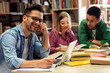 © Zoran Zeremski - Three young students study in the school library, male student sitting in front of laptop and looking at camera.