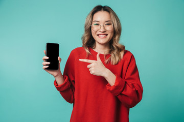 Happy young woman posing isolated over blue wall background showing display of mobile phone.