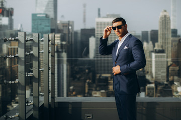 Wall Mural - A handsome man wearing glasses in a classic suit wears a background of modern buildings