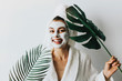 © ClaudiK - woman has fun with a facial mask.Young girl with facial mask, holding bottles of cream  looking at camera over white background. Cosmetic procedure. Beauty spa and cosmetology.Spa Facial Mask. Spa day