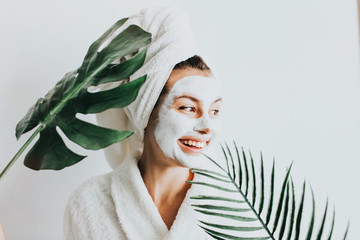 young beautiful woman in face mask of therapeutic white mud and tropical leaves. spa treatment, self