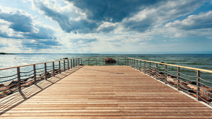 Perspective view at sea from center of wooden pier made of deck board  with posts and ropes. Dramatic blue sky at beautiful sunny day