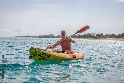Elder fit man is kayaking on a bright yellow kayak in Caribbean Sea during a sunny summer day Canvas Print