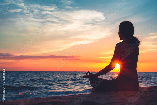 Silhouette young woman practicing yoga on the beach at sunset. Fototapeta