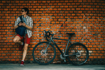 A young stylish man posing next to his bicycle.