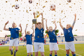 Happy Boys Celebrating Soccer Championship. Youth Football Winning Team Jumping and Rising Golden Cup on Trophy Ceremony After the Final Tournament Game. Football Stadium and Fans in the Background