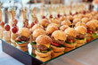 © mirage_studio - Buffet table with mini hamburgers and canape at luxury wedding reception, copy space. Serving food and appetizers at restaurant. Catering banquet table