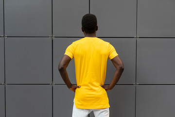Wall Mural - Empty blank yellow t-shirt on the american male back standing near wall, mockup design