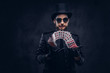 © Fxquadro - Magician in a black suit, sunglasses and top hat, showing trick with playing cards on a dark background.