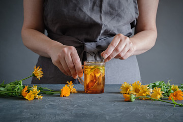 Woman making healthy tea with calendula or marigold flowers.