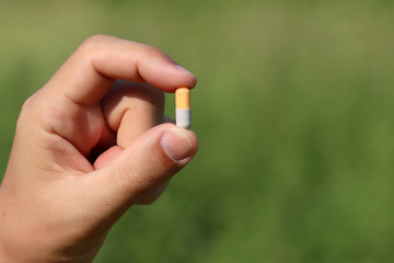 Capsule in male hand on blurred green nature background, man holding pill close up. Concept of pharmacy, treatment, vitamins, health care