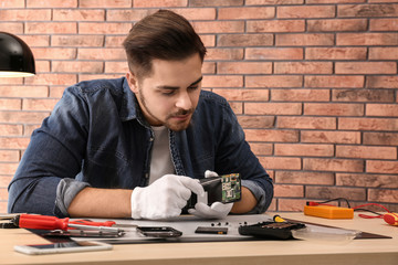 Wall Mural - Technician repairing broken smartphone at table in workshop. Space for text