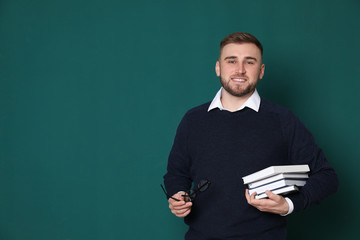 Wall Mural - Portrait of young teacher with books and glasses on green background. Space for text