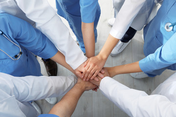 Team of medical workers holding hands together indoors, top view. Unity concept