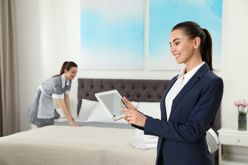 Sticker - Housekeeping manager with tablet checking maid work in hotel room. Space for text