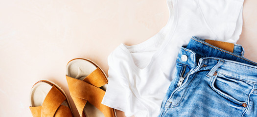 Woman's casual summer vacation outfits with white t-shirts, denim shorts, trendy leather sandals, with crisscross details on pink pastel background. Flat lay.
