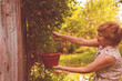 © Mihail - female worker hanging a pot with a plant flower, small business concept