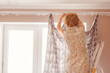 © Mihail - adult housewife hanging the curtains standing on the ladder at home