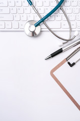 Stethoscope on keyboard on white table background. Online medical information treatment technology office concept, top view, flat lay, copy space
