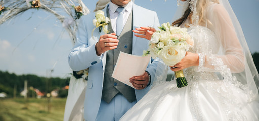 Wall Mural - Couple is walking at the wedding ceremony outdoors. Bride and groom holding arms. Arch with flowers.