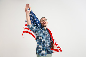 Celebrating an Independence day. Stars and Stripes. Young man with the flag of the United States of America isolated on white studio background. Looks crazy happy and proud as a patriot of his country